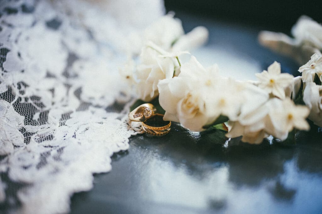 Window lit, detail shot of bride's wedding dress, flower crown, and the couple's rings.